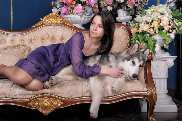 花が付いているつぼの中でソファに女の子ティーンと犬マラミュート — ストック写真