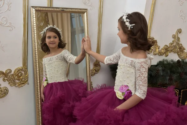 ワインレッドのドレスでシックな白いドレスの少女は鏡に立ち彼女の反射で見える — ストック写真