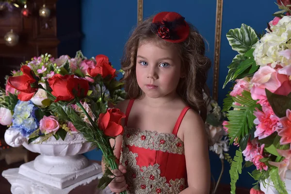 一个小公主女孩的肖像在红色礼服与鲜花在她的手中 她周围 — 图库照片