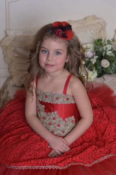 一个穿着红色礼服的小女孩公主的肖像和坐在沙发上的帽子 — 图库照片