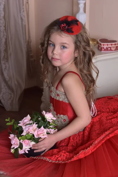 一个穿着红色礼服和帽子的小女孩公主的画像坐在沙发上 上面有一盒玫瑰 — 图库照片