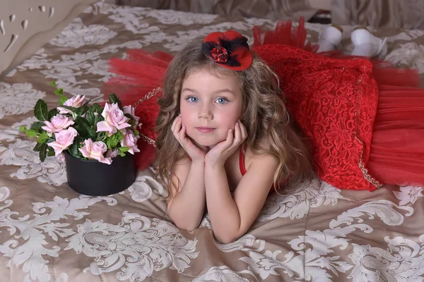 一个穿着红色礼服和帽子的小女孩公主的画像坐在沙发上 上面有一盒玫瑰 — 图库照片