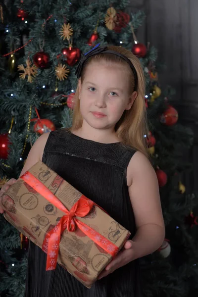 女孩金发碧眼的孩子在一个黑色的礼服与礼物在圣诞树上 — 图库照片