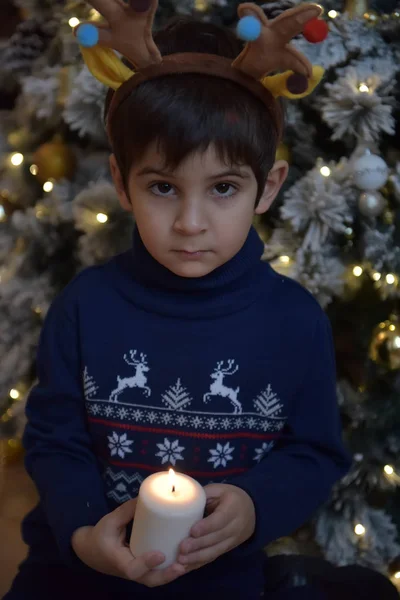 鹿の角と彼の手のキャンドル クリスマス ツリーで青いセーターの少年 — ストック写真