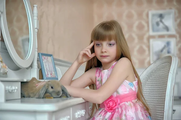 一个穿着粉色衣服的年轻金发女郎早上坐在镜子旁边的梳妆台旁 — 图库照片