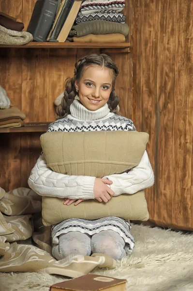 セーターに座っている枕を抱き締めるお下げの女の子 — ストック写真