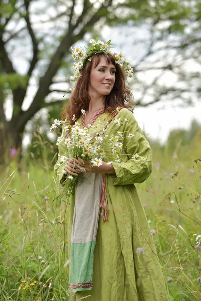 Mujer en un vestido verde con una corona de margaritas en el pelo y — Foto de Stock