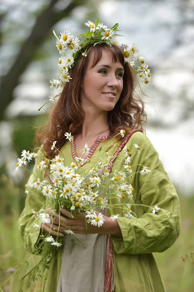 Mulher em um vestido verde com uma coroa de margaridas em seu cabelo e — Fotografia de Stock
