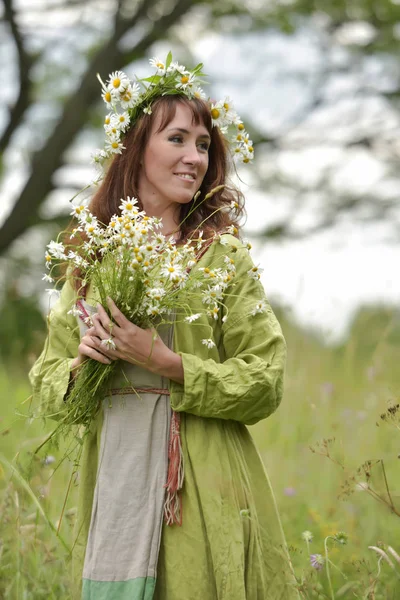 Mulher em um vestido verde com uma coroa de margaridas em seu cabelo e — Fotografia de Stock