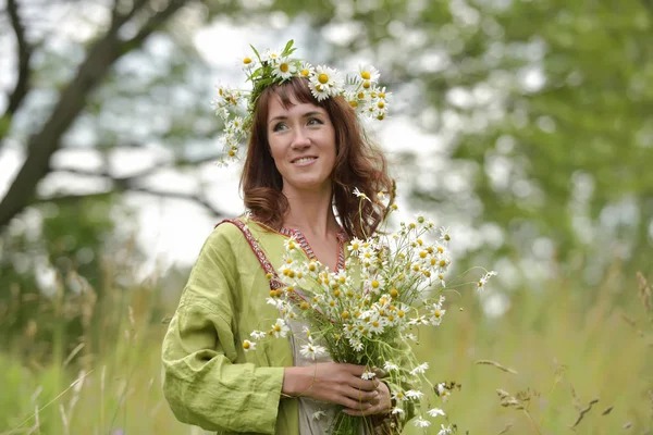 Woman in a green dress with a wreath of daisies in her hair and — Stock Photo, Image