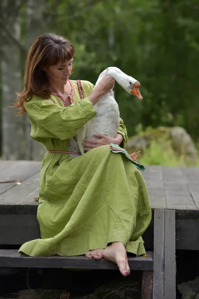 Kvinna i grön klänning med en gås i famnen — Stockfoto