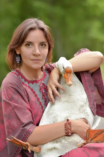 Woman in burgundy dress on a farm with a goose — ストック写真