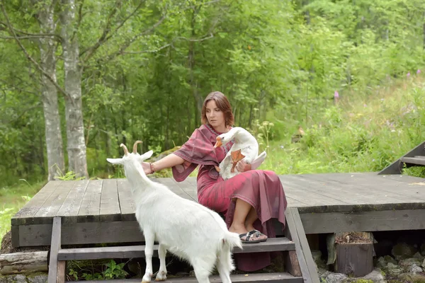 Woman in a burgundy dress on a farm with a goose in her arms and — 스톡 사진