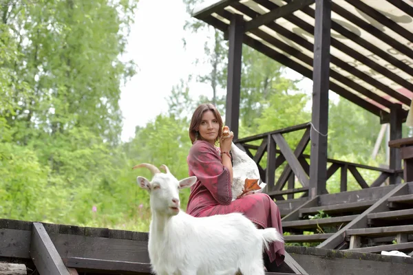 Frau in weinrotem Kleid auf einem Bauernhof mit einer Gans im Arm und — Stockfoto