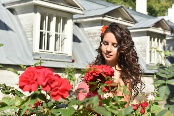 Vacker flicka med lockar bredvid röda rosor i trädgården — Stockfoto