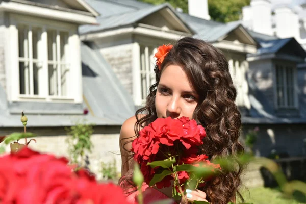 Belle fille avec des boucles à côté de roses rouges dans le jardin — Photo