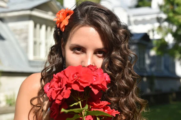 Hermosa chica con rizos junto a rosas rojas en el jardín — Foto de Stock