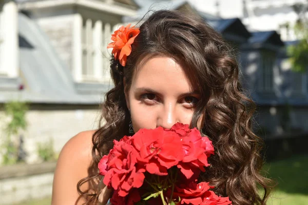 Hermosa chica con rizos junto a rosas rojas en el jardín —  Fotos de Stock