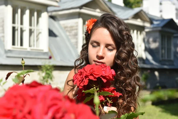 Gyönyörű lány fürtök mellett vörös rózsa a kertben — Stock Fotó