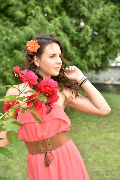 Piękna dziewczyna z loki obok czerwonych róż w ogrodzie — Zdjęcie stockowe