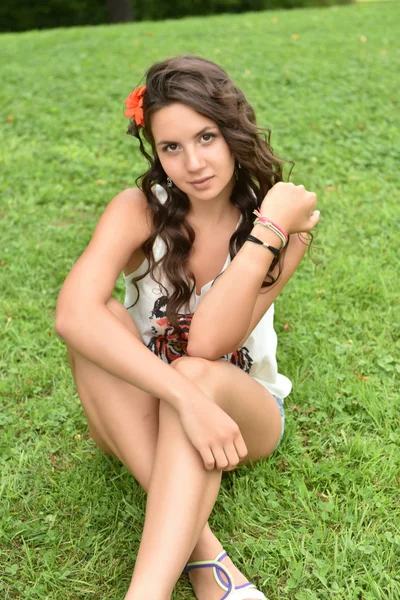 Красивая девушка брюнетка, сидящая на лавке на зеленой траве — стоковое фото