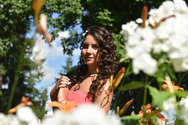 Brunette with curly hair in the summer among the flowers — Stock Photo, Image