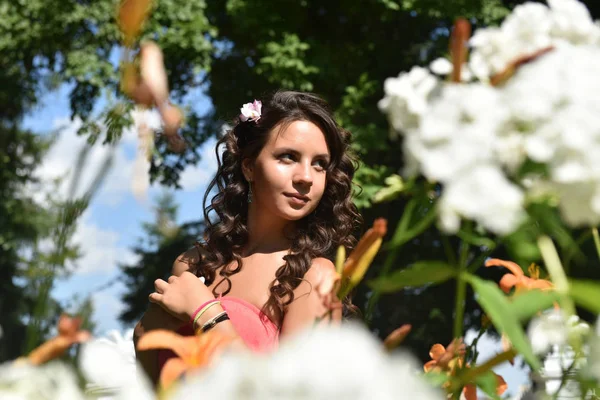 Brunette with curly hair in the summer among the flowers — Stock Photo, Image
