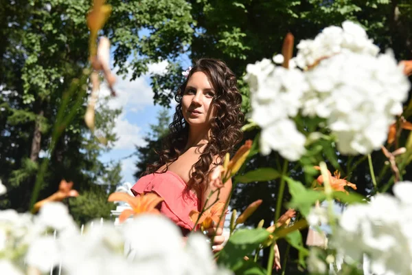 Brunette met krullend haar in de zomer onder de bloemen — Stockfoto