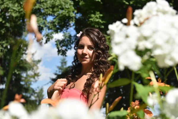 Brünette mit lockigem Haar im Sommer zwischen den Blumen — Stockfoto