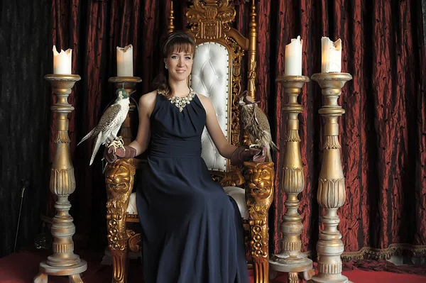 Elegante bruna in abito nero da sera su un trono con falchi — Foto Stock