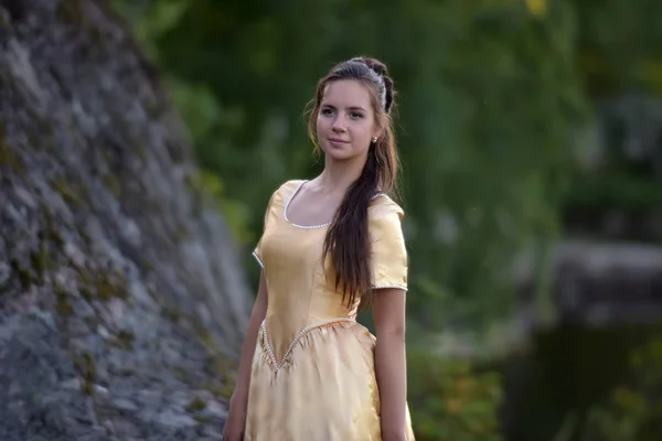 Beautiful young princess brunette in a golden dress in the park — Stock Photo, Image