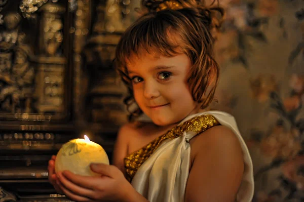 Portrait of a smiling little girl in an antique tunic with candl — Stock Photo, Image