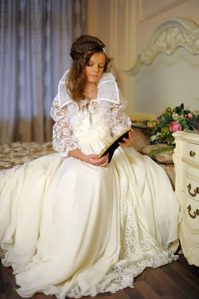 Piękna dziewczyna w długiej białej sukni siedzącej na łóżku — Zdjęcie stockowe