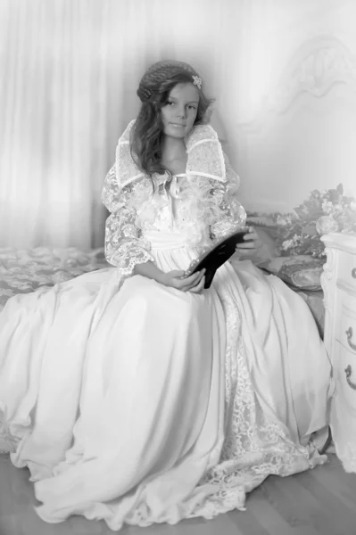 Hermosa chica en un vestido blanco largo sentado en la cama —  Fotos de Stock