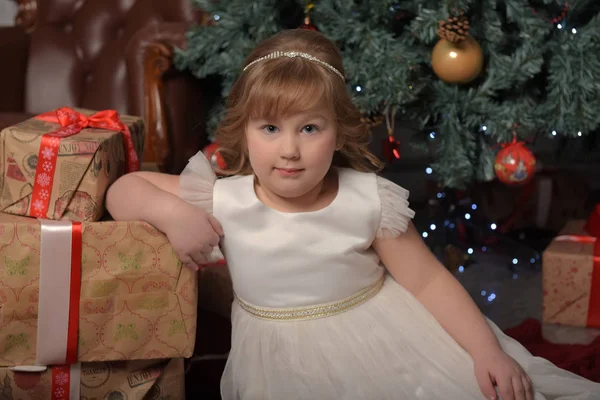 Chica en vestido blanco sentado en el árbol de Navidad con regalos —  Fotos de Stock