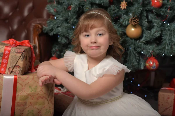 Meisje in witte jurk zittend op de kerstboom met geschenken — Stockfoto