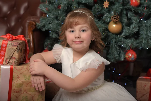 Chica en vestido blanco sentado en el árbol de Navidad con regalos —  Fotos de Stock