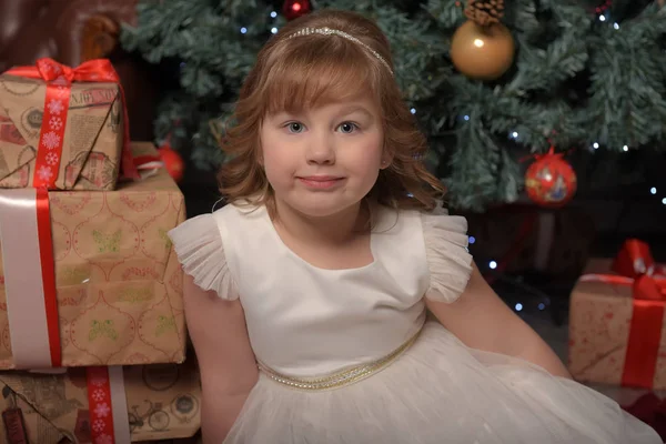 Lány fehér ruhában ül a karácsonyfát ajándékokkal — Stock Fotó
