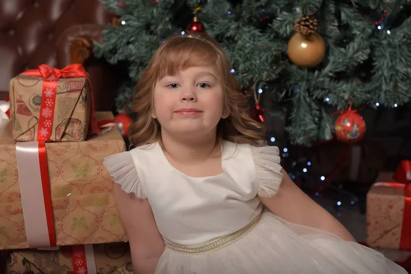 Chica en vestido blanco sentado en el árbol de Navidad con regalos — Foto de Stock
