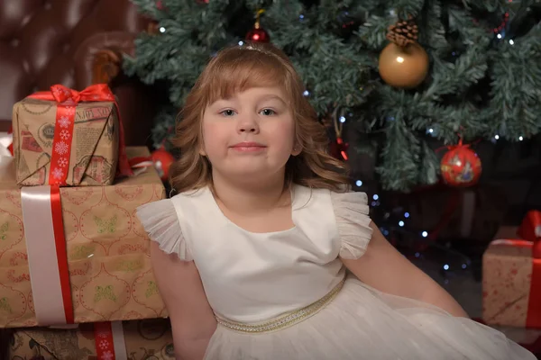 Chica en vestido blanco sentado en el árbol de Navidad con regalos —  Fotos de Stock