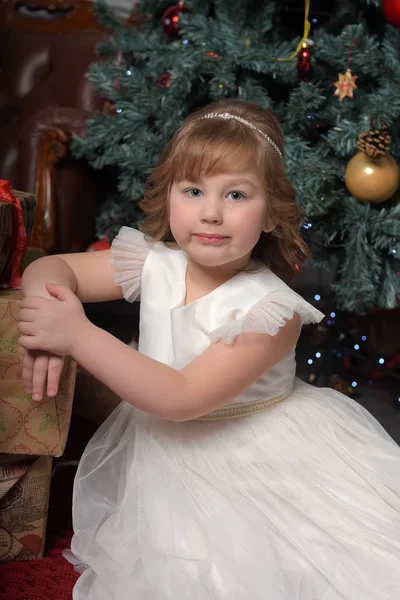 Chica en vestido blanco sentado en el árbol de Navidad con regalos — Foto de Stock