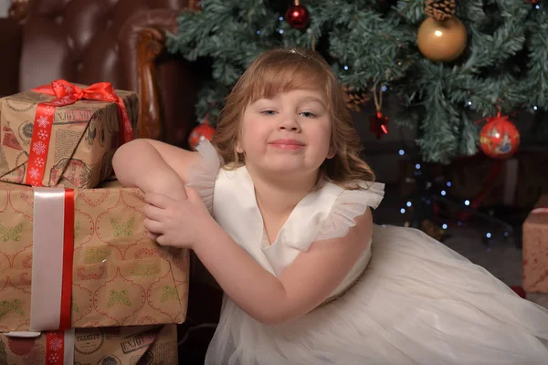 Chica en vestido blanco sentado en el árbol de Navidad con regalos —  Fotos de Stock