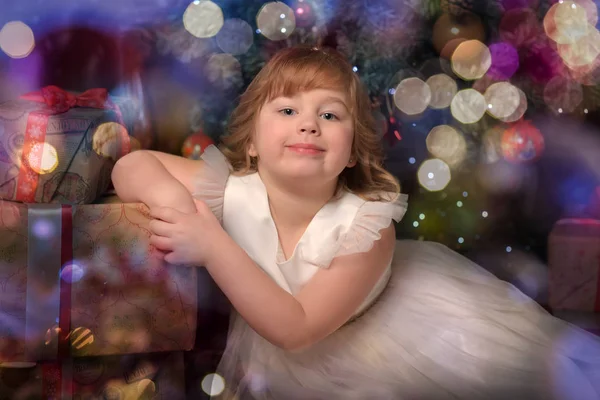 Chica en vestido blanco sentado en el árbol de Navidad con regalos — Foto de Stock