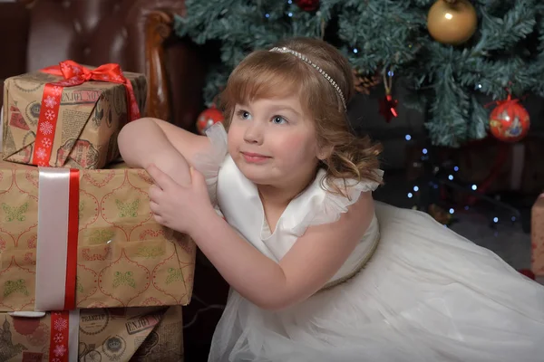 Ragazza in abito bianco seduta sull'albero di Natale con regali — Foto Stock