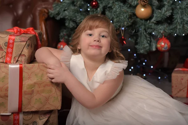 Menina em vestido branco sentado na árvore de Natal com presentes — Fotografia de Stock