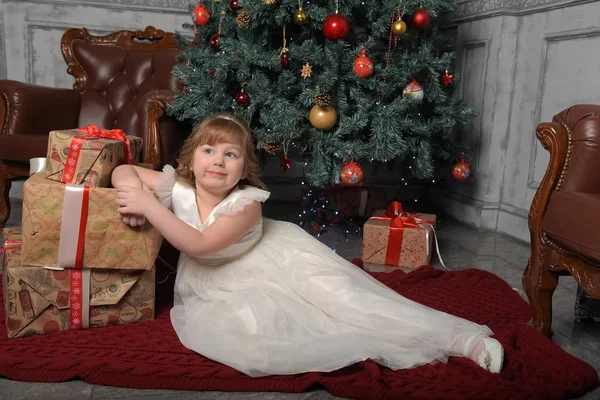 Chica en vestido blanco sentado en el árbol de Navidad con regalos —  Fotos de Stock