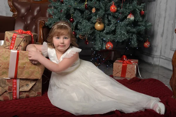 Menina em vestido branco sentado na árvore de Natal com presentes — Fotografia de Stock