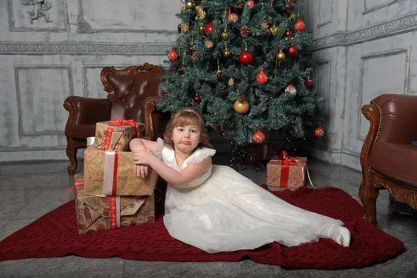 Flicka i vit klänning sitter på julgran med gåvor — Stockfoto