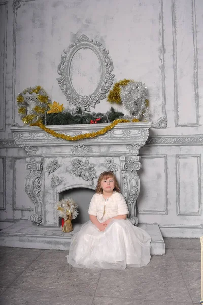 Girl in a white dress and a fur coat by the old fireplace in the — Stock Photo, Image