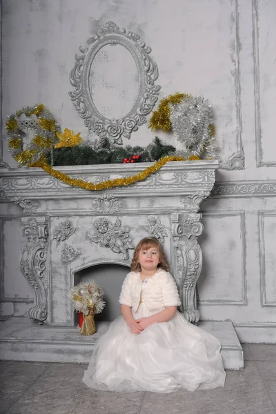 Menina em um vestido branco e um casaco de pele pela velha lareira no — Fotografia de Stock